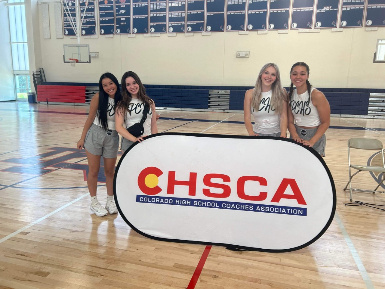 Senior Cheerleaders standing next to a banner that says, "CHSCA Colorado High School Coaches Association"